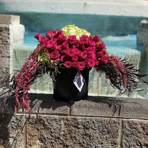 Deep red roses with green hydrangea and trailing amaranthus by a stone fountain at Raleigh flower studio