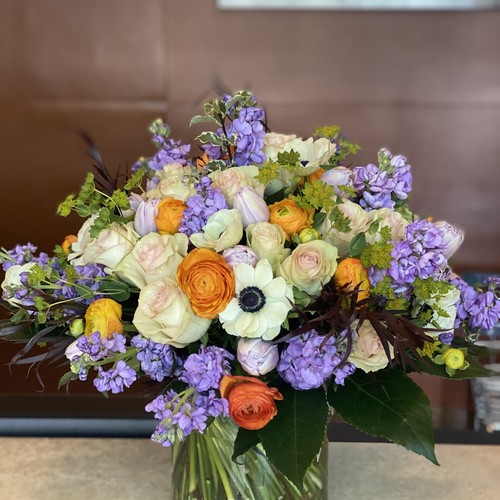 White roses orange ranunculus and purple stock in a glass vase from Raleigh flower studio